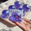 A hand holds a clear plastic squishy bubble squid stress relief toy with purple and pink accents.