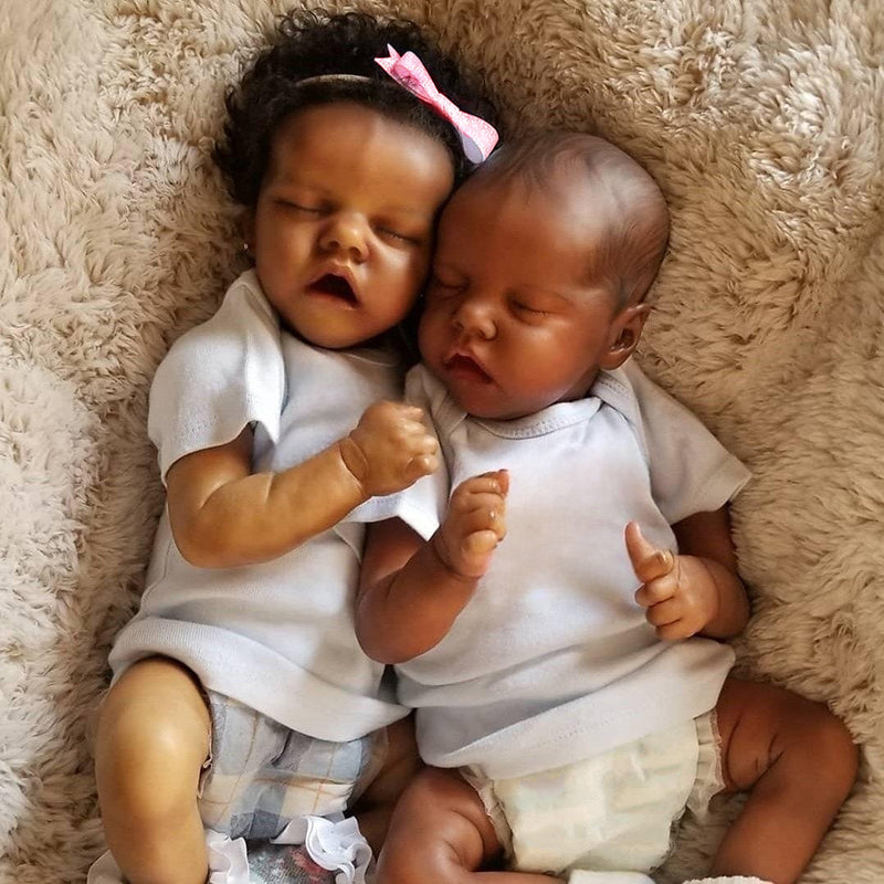 A newborn twin baby doll with dark skin is lying on a fluffy beige surface.