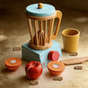 A wooden kitchen play set featuring a juice press, cup, knife, and orange for children's play.