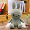 A soft, light green Miffy plush toy rabbit standing upright on a wooden surface.