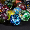 A close-up shot of a set of seven polyhedral resin dice in various colors and shapes on a dark surface.