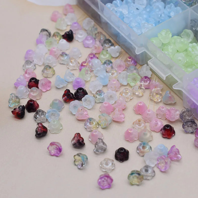 A collection of colorful glass beads in various shades of pink, purple, and green are displayed next to a plastic container.
