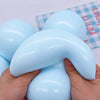 A hand is squeezing a light blue slow rising squishy ball stress relief fidget toy against a checkered background.