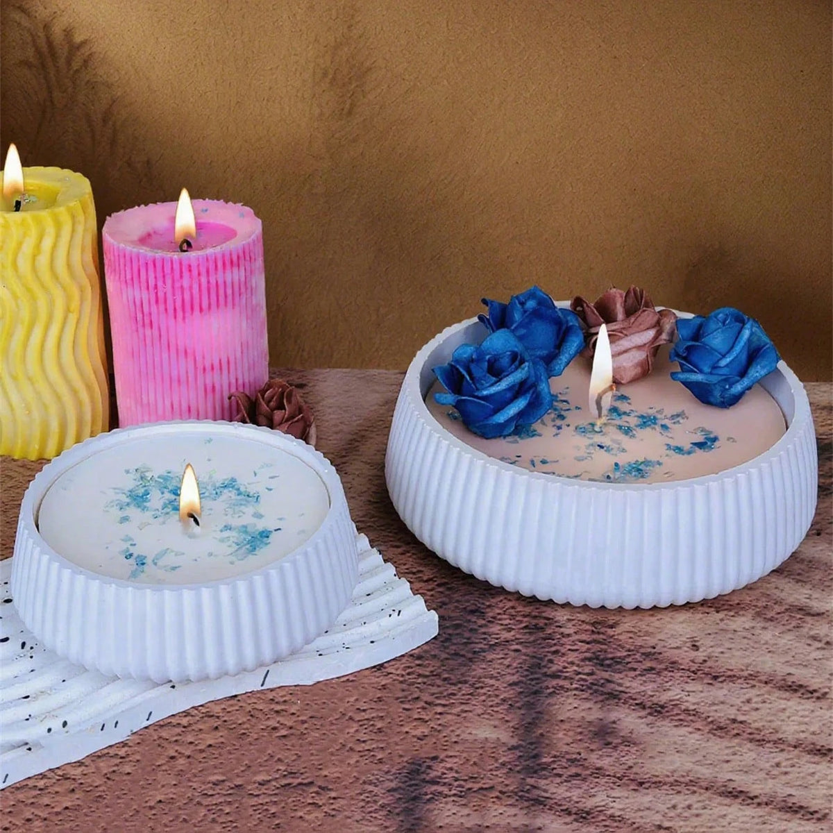 A collection of candles and blue fabric roses displayed on a wooden surface.