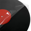 A black vinyl record disc is partially visible, covered by a clear self-adhesive sleeve with a red center label.