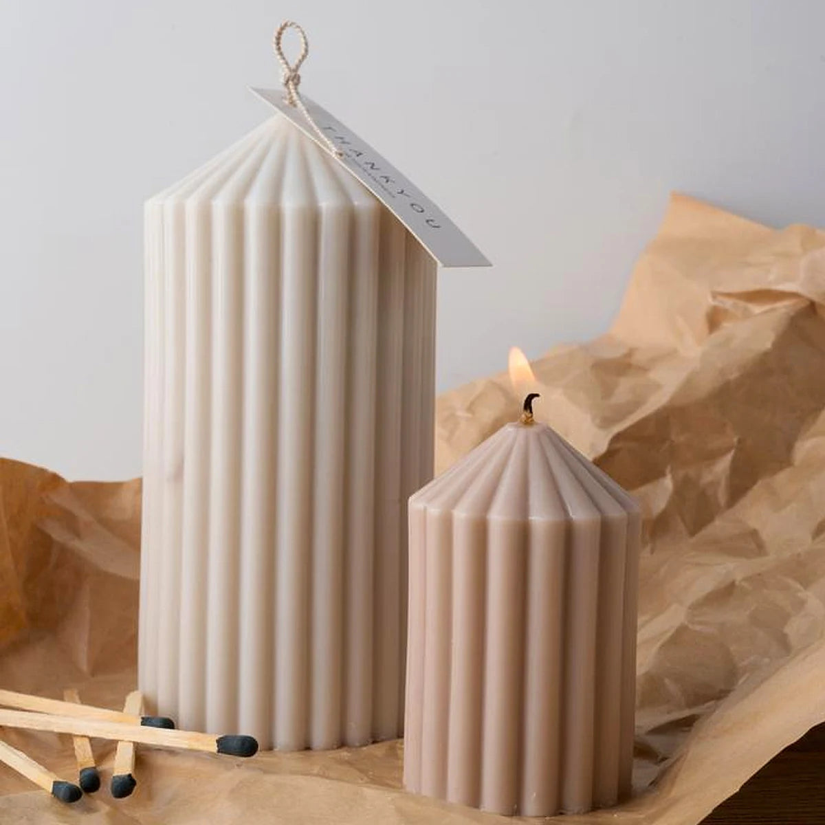 A tall, cylindrical silicone candle holder with vertical stripes stands next to a smaller one and tissue paper.