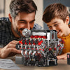 A man and a boy are assembling a detailed motorized V8 supercar engine building kit on a table.