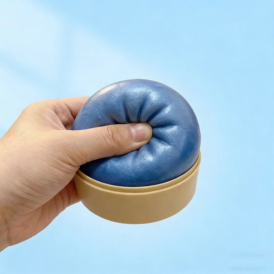 A hand holds a blue squishy toy shaped like a dumpling in a beige container against a light blue background.