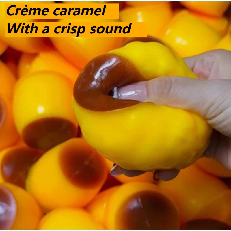 A hand squeezes a bright yellow, squishy pudding stress ball with a brown tint.