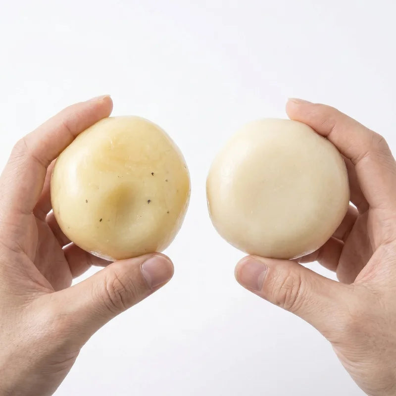 A hand holds a smooth, pale yellow mashed potato squeeze toy stress reliever.