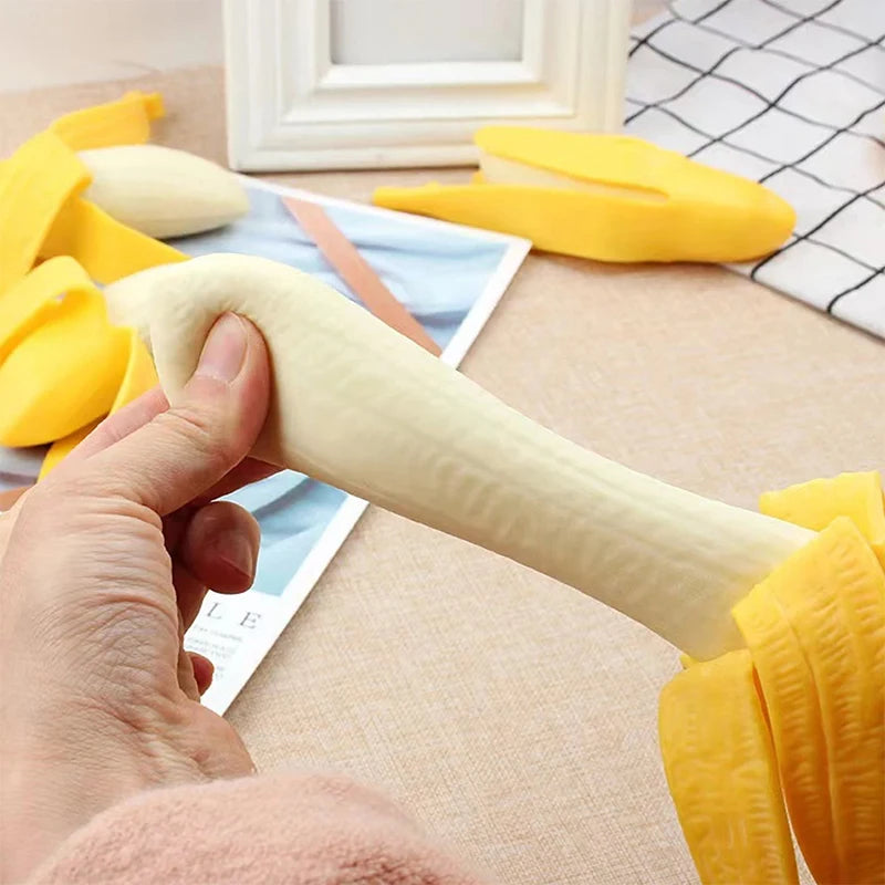 A hand is holding a beige stretchy banana-shaped fidget toy next to yellow silicone stress relief toys.