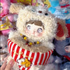 A fluffy white plush doll wearing a hood and striped clothing is held in a hand.