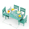 A miniature dollhouse furniture set featuring green wooden chairs and a table with dishes and glassware.
