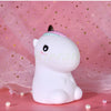 A white unicorn LED night light with a pink horn resting on a pink surface.