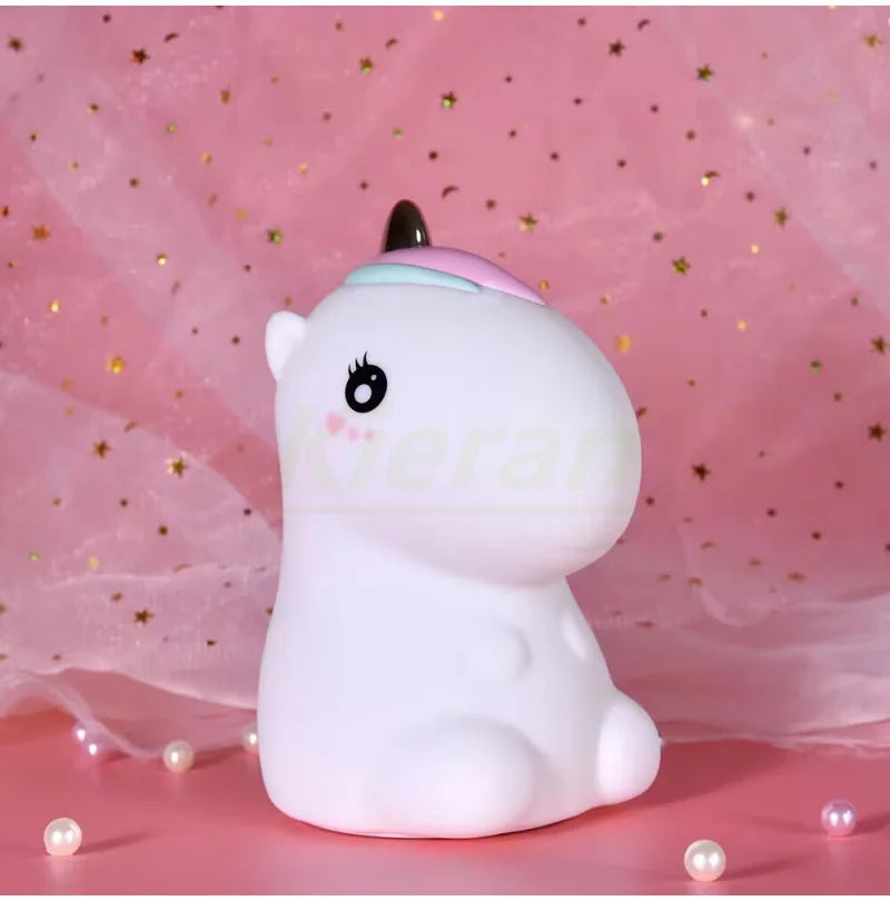 A white unicorn LED night light with a pink horn resting on a pink surface.