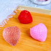 Two squishy strawberry fidget toys, one red and one pink, are displayed on a wooden surface.