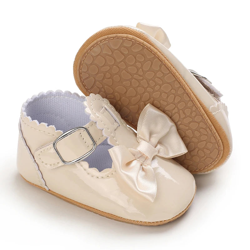 A pair of light beige lace-trimmed baby girl moccasin shoes with a bow shown from the top and side.
