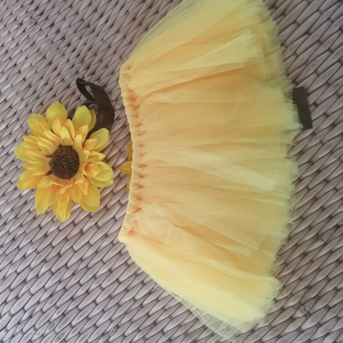 A yellow tulle tutu skirt and headdress set displayed on a woven mat.