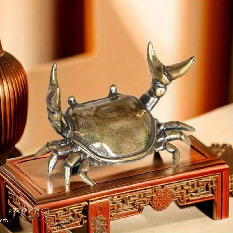 A brass crab figurine statue resting on a wooden box.