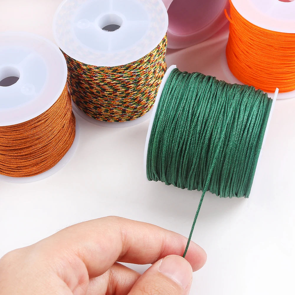A hand holds a spool of green macrame cord for jewelry making and crafts, surrounded by other colored cords.