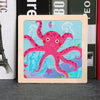 A wooden tangram puzzle featuring a pink octopus design on a light blue background.