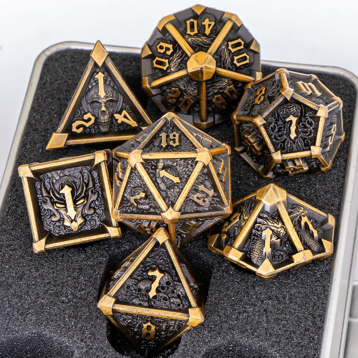 A set of seven metal dice featuring skull and dragon designs displayed in a dark container.
