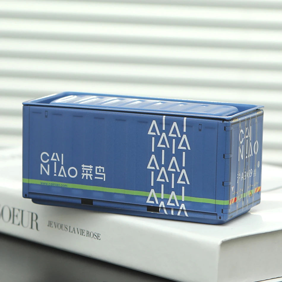 A blue miniature industrial iron storage box with an openable lid resting on a white book.