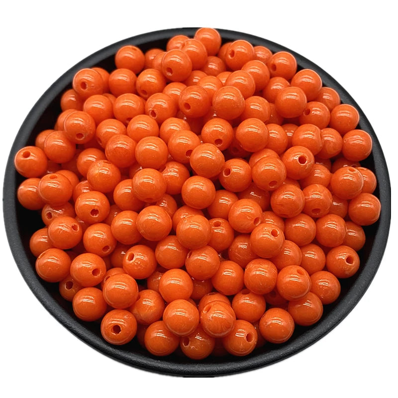 A pile of small, round, orange acrylic beads for jewelry making in a black bowl.