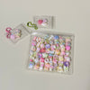 A clear plastic container filled with various pastel-colored squishy fidget toys and a small green beaded chain.