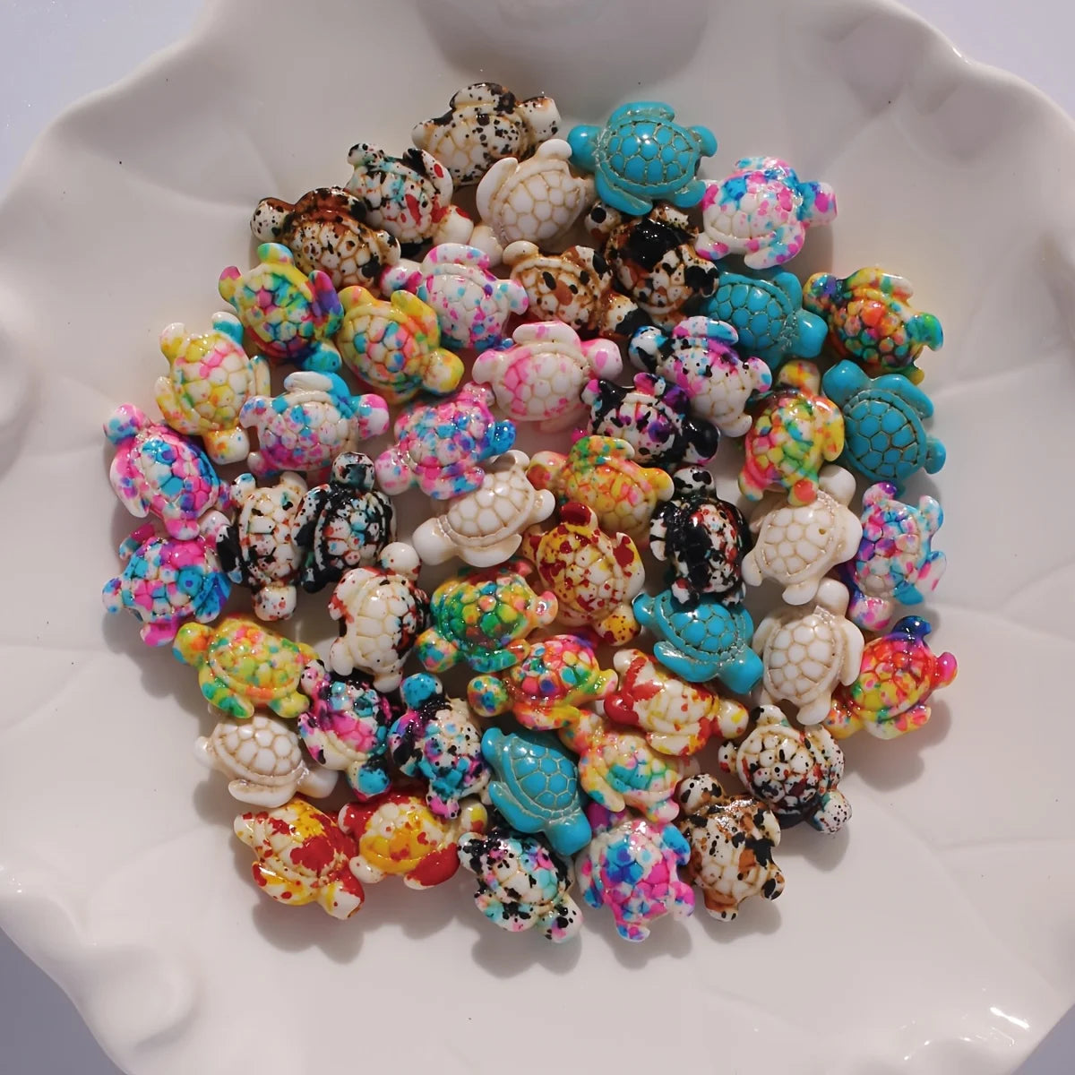 A pile of colorful ocean turtle beads in various shades of pink, blue, yellow, and white on a white plate.