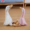 A white and pink long neck goose plush doll sitting on a wooden floor.