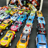 A collection of die-cast mini racing cars in various colors and liveries displayed in a white storage box.