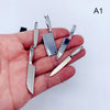 A set of miniature metal kitchen knives for a dollhouse, held in a person's hand.