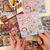 A close-up of a pink and blue embroidery-style sticker book featuring cute food characters and patterns.