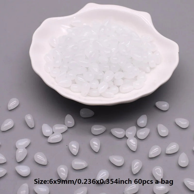 A white ceramic dish filled with small, translucent water drop glass beads for jewelry making