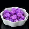A white bowl filled with purple acrylic pearl beads for jewelry making