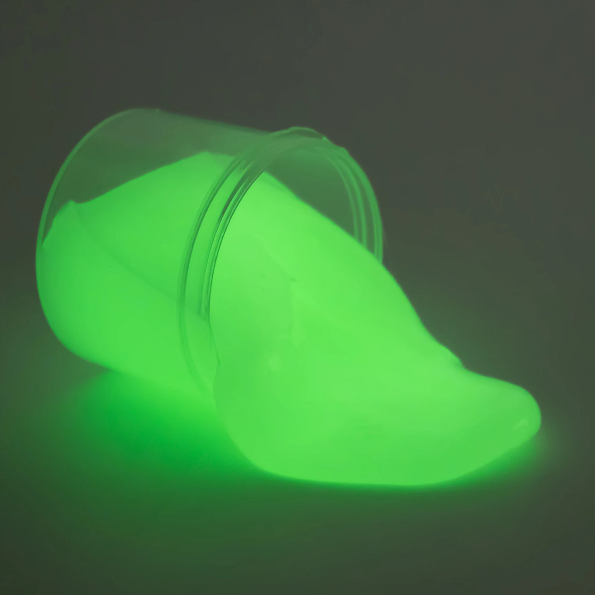 A translucent, lime green glow-in-the-dark crystal slime resting on a dark surface.