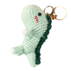 Handmade crochet dinosaur keychain in light green with a pink mark, attached to a gold-colored split ring.