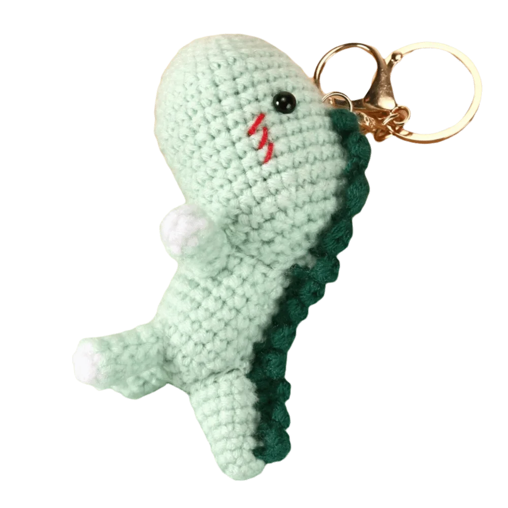 Handmade crochet dinosaur keychain in light green with a pink mark, attached to a gold-colored split ring.