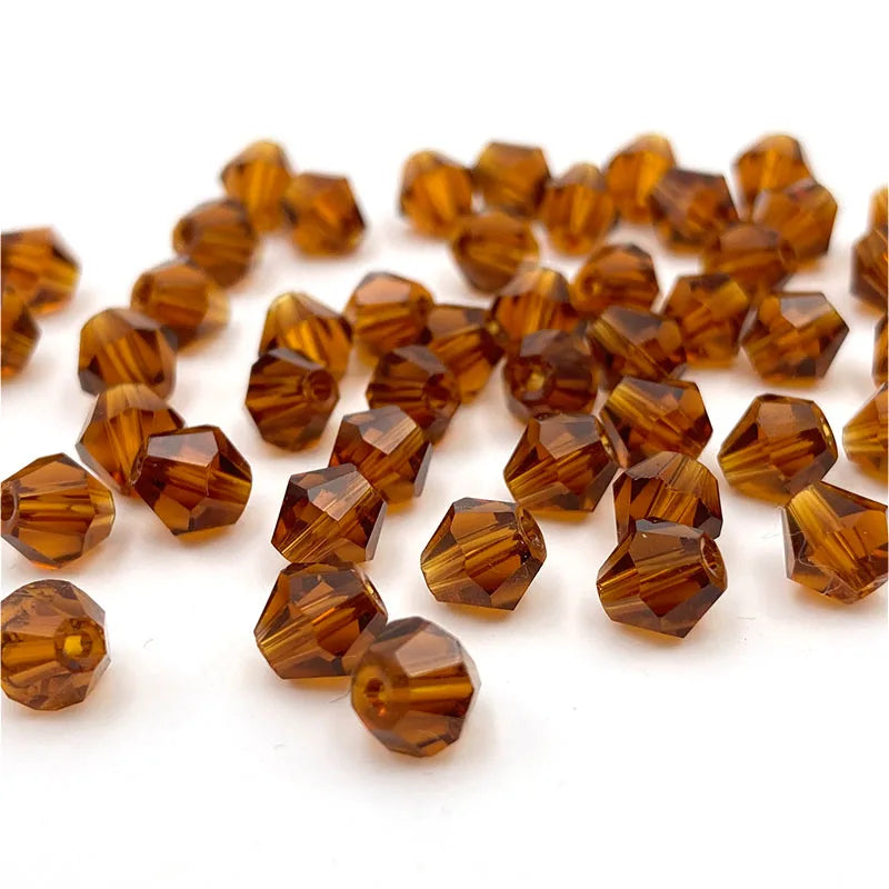 A pile of faceted bicone crystal glass beads in amber and brown tones for jewelry making.
