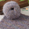 A ball of soft purple gray alpaca blend yarn resting on a knitted fabric background.