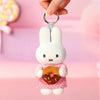 A white bunny plush keychain charm with pink accents and a donut detail is being held by a hand.