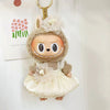 A small doll wearing a light beige outfit with a floral headpiece and a ruffled skirt.