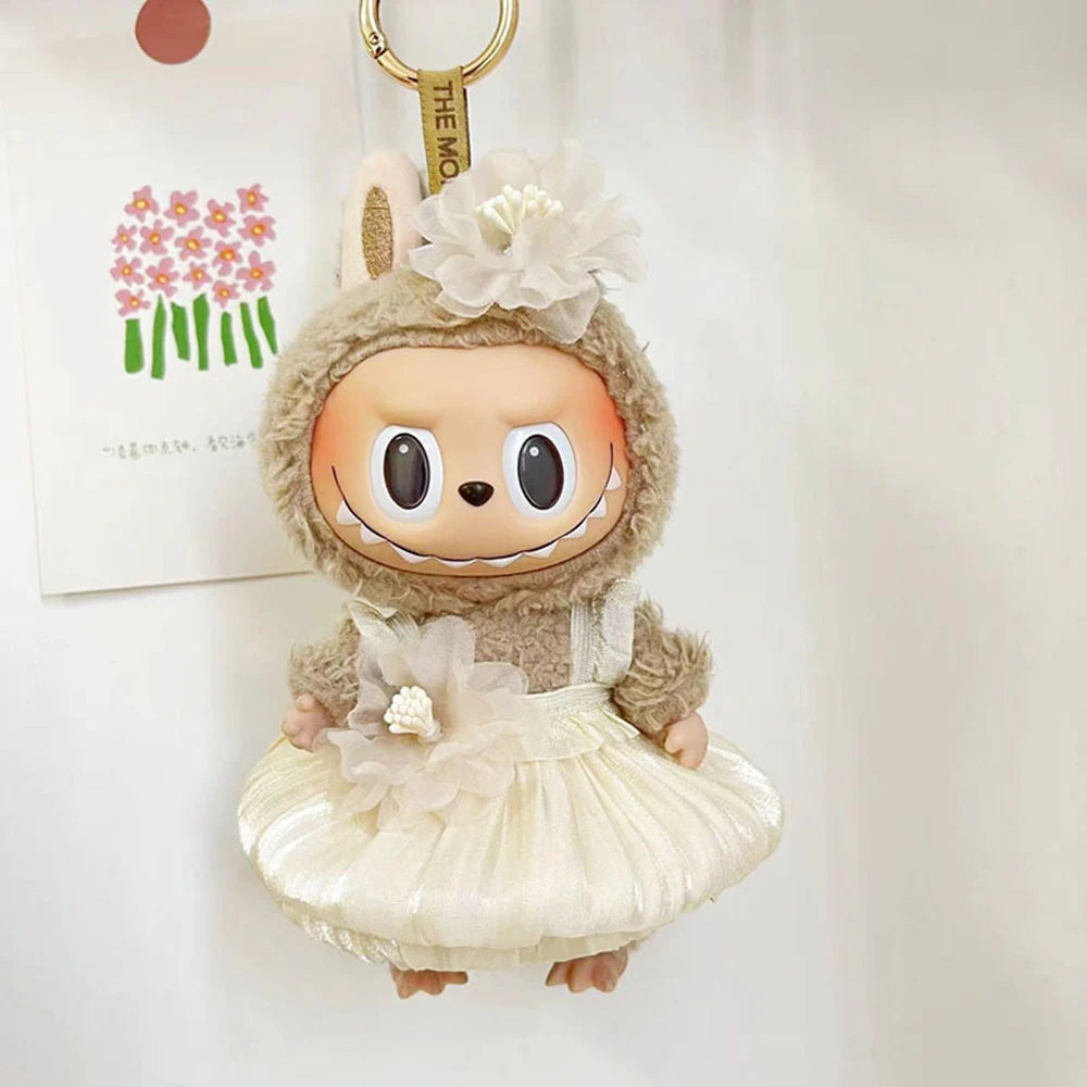 A small doll wearing a light beige outfit with a floral headpiece and a ruffled skirt.