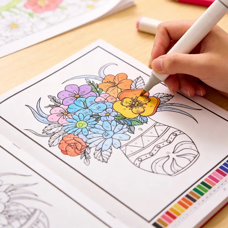A hand is coloring a botanical illustration in a coloring book with various colored pencils.