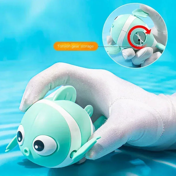 A hand holds a light green clockwork fish bath toy for babies, demonstrating its storage feature.