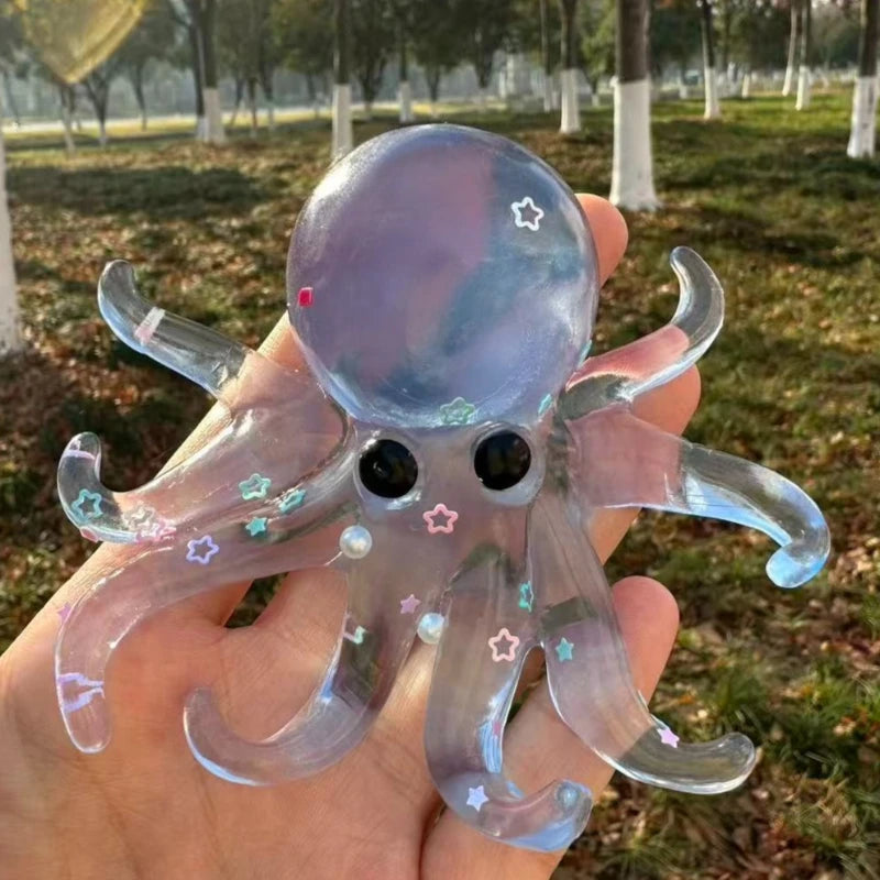 A hand holds a clear silicone octopus fidget toy with purple and pink glitter stars.