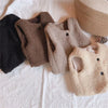 A collection of beige and brown lamb wool vests for children displayed on a white surface.