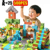 A smiling child is holding up a large structure built from colorful magnetic building tiles.