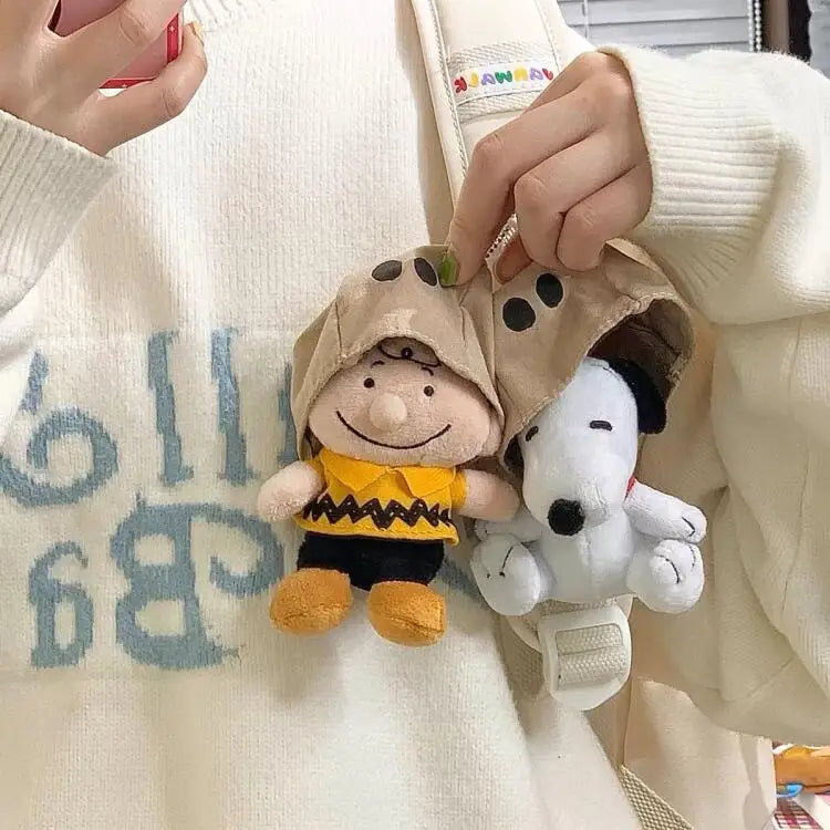 A plush Snoopy character wearing a brown hood is being held by a person against a white sweater.
